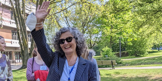 Ute Ritterfeld steht winkend auf einer Wiese vor Bäumen auf dem Campus der TU